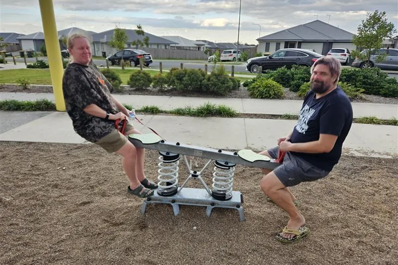 Two participants using outdoor exercise equipment at a local park